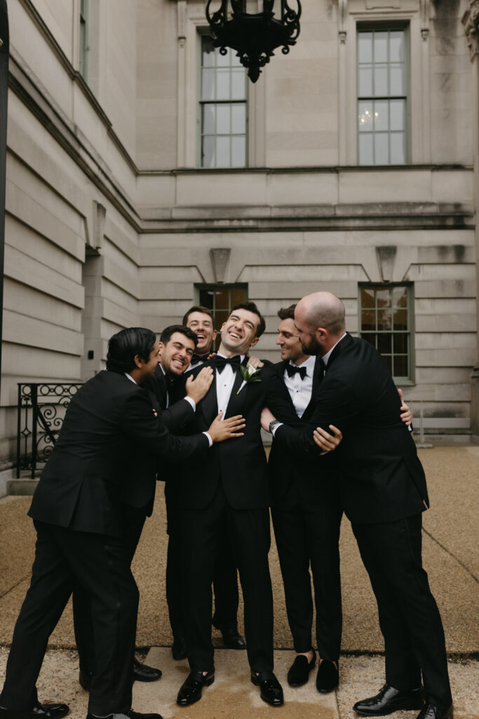 Groom and Groomsmen hugging in formal black tie attire posing in front of the Larz Anderson House