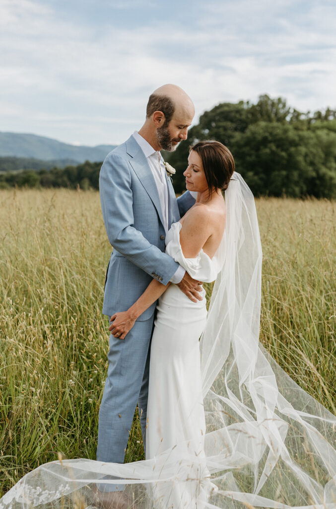 Bride and groom embracing in a scenic field with the Blue Ridge Mountains in the distance.