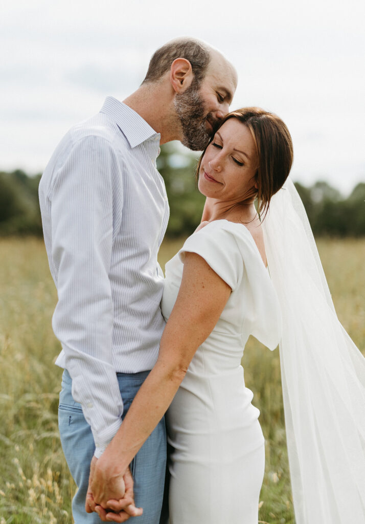 Bride and groom embracing in a scenic field with the Blue Ridge Mountains in the distance.