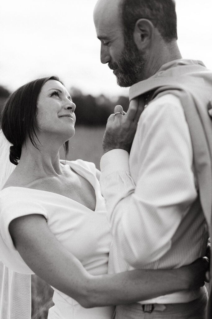 Bride and groom embracing in a scenic field with the Blue Ridge Mountains in the distance.