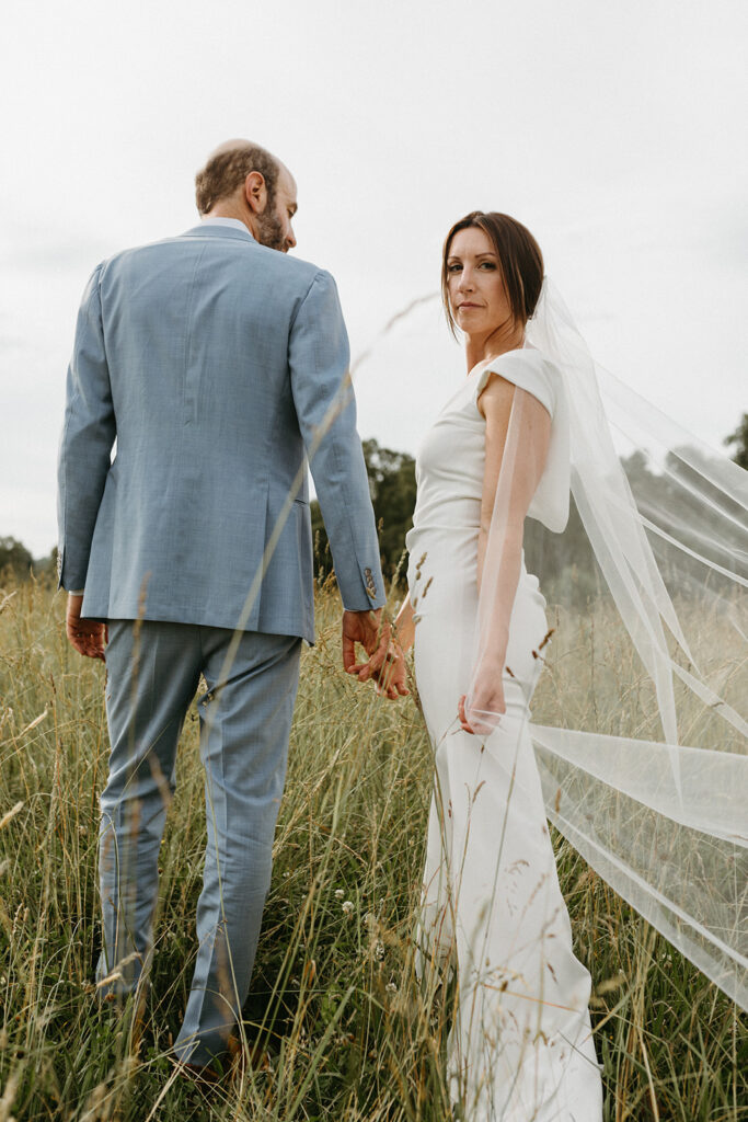 Bride and groom embracing in a scenic field with the Blue Ridge Mountains in the distance.