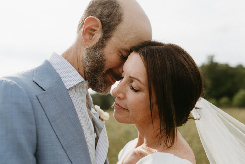Bride and groom embracing in a scenic field with the Blue Ridge Mountains in the distance.