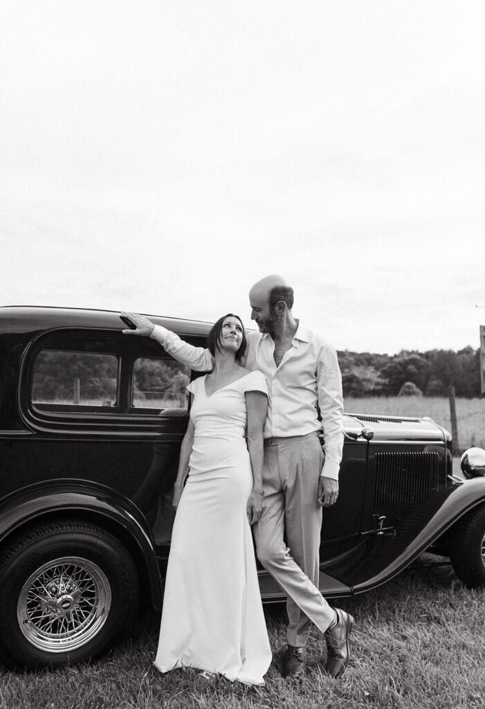 Bride and Groom portrait in front of a vintage car, in a scenic field with the Blue Ridge Mountains in the distance.