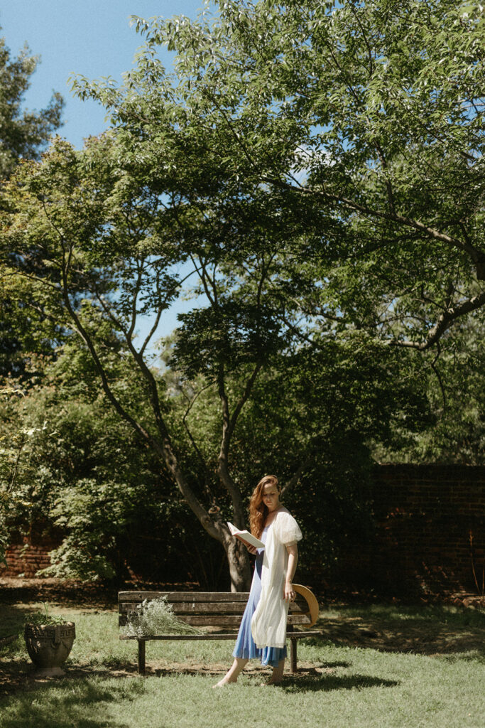 Portrait of woman in vintage dress and robe reading a book in the garden at the Branch Museum in Richmond, Virginia. 