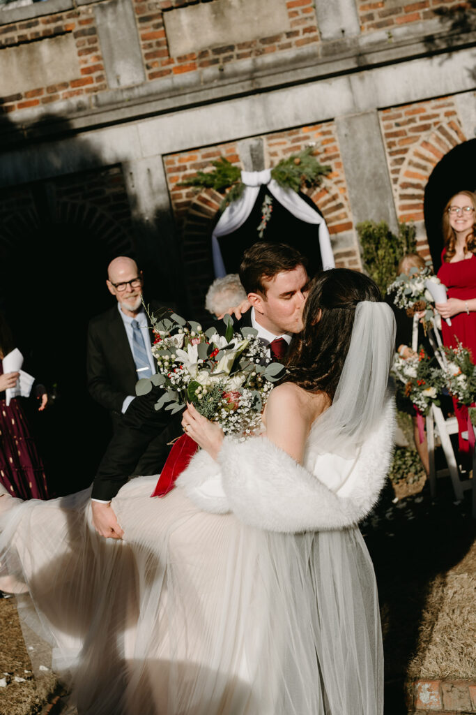 Newlyweds kissing in the aisle with guests tossing flower petals at their Richmond winter micro wedding.