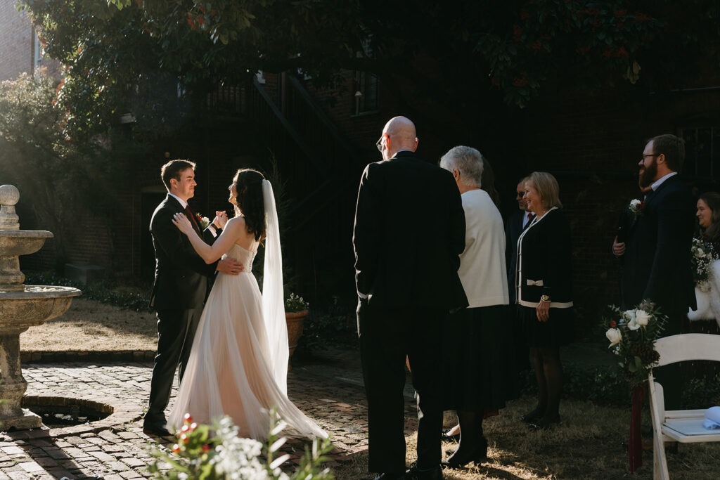 Bride and groom having their first dance in the courtyard as family watches. 
