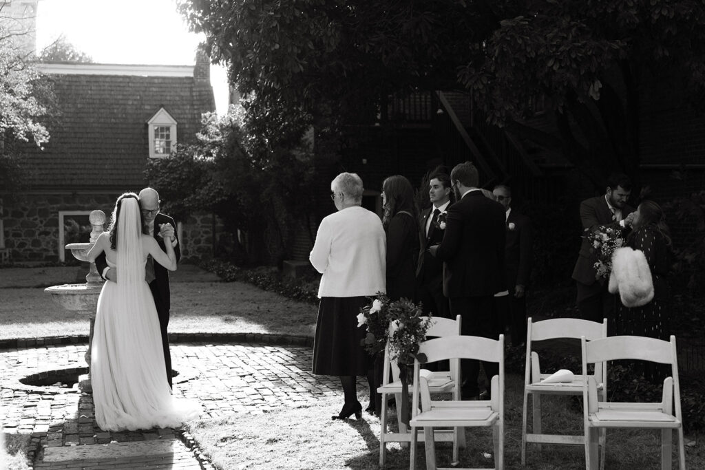 Bride dancing with dad in the courtyard as family watches. 