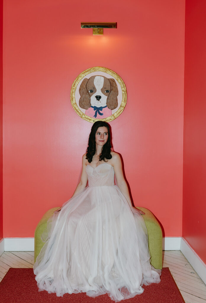 Bride portrait of her sitting on a green bench against a pink wall at Quirk Hotel before the couple's first look. 